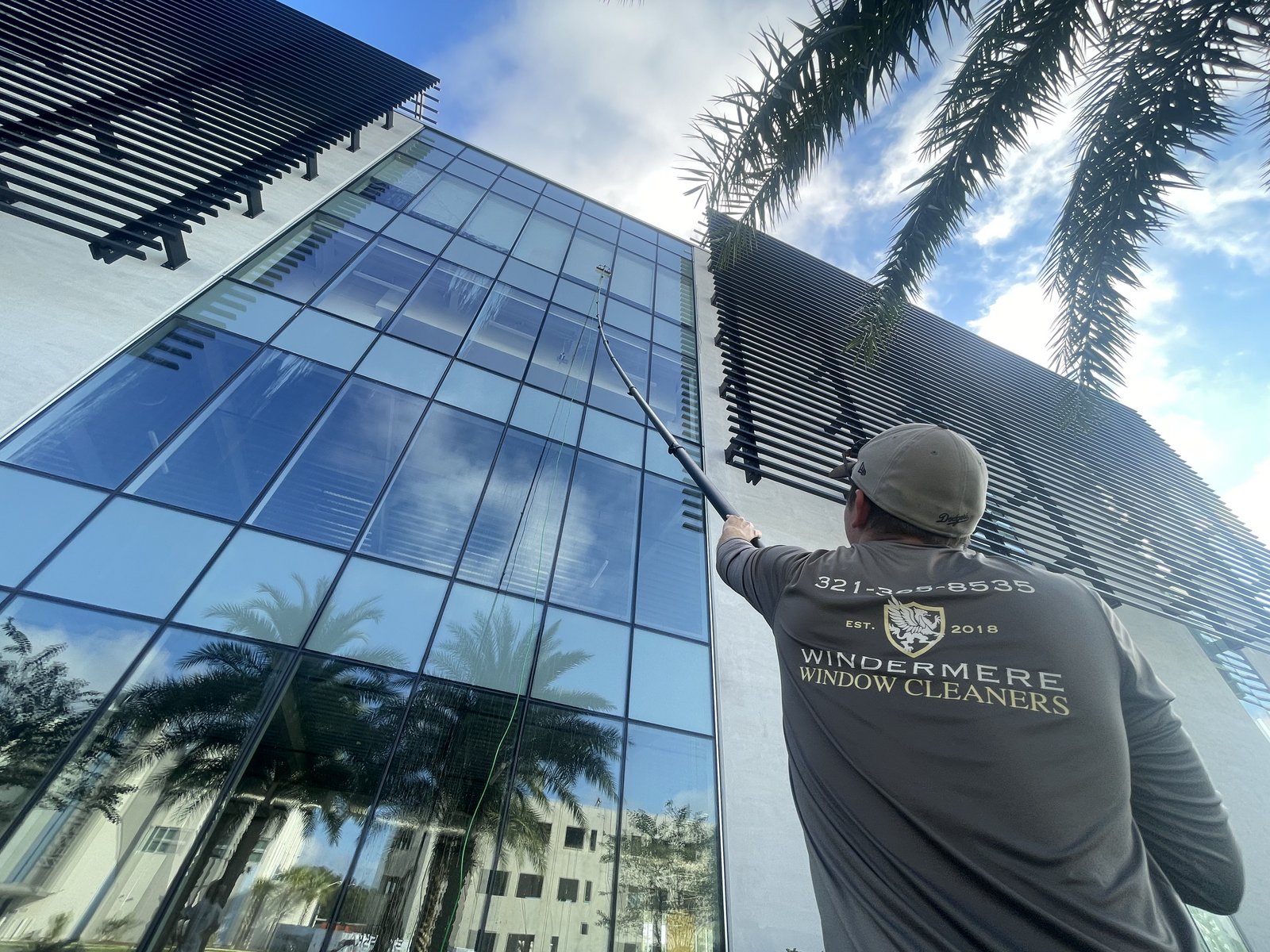 Technician cleaning glass on a modern building with a water-fed pole